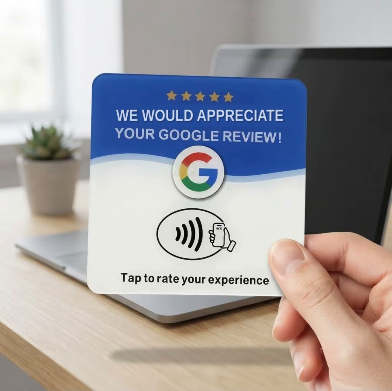 A hand holding the blue FiveStarTap review card in front of a laptop on a desk.